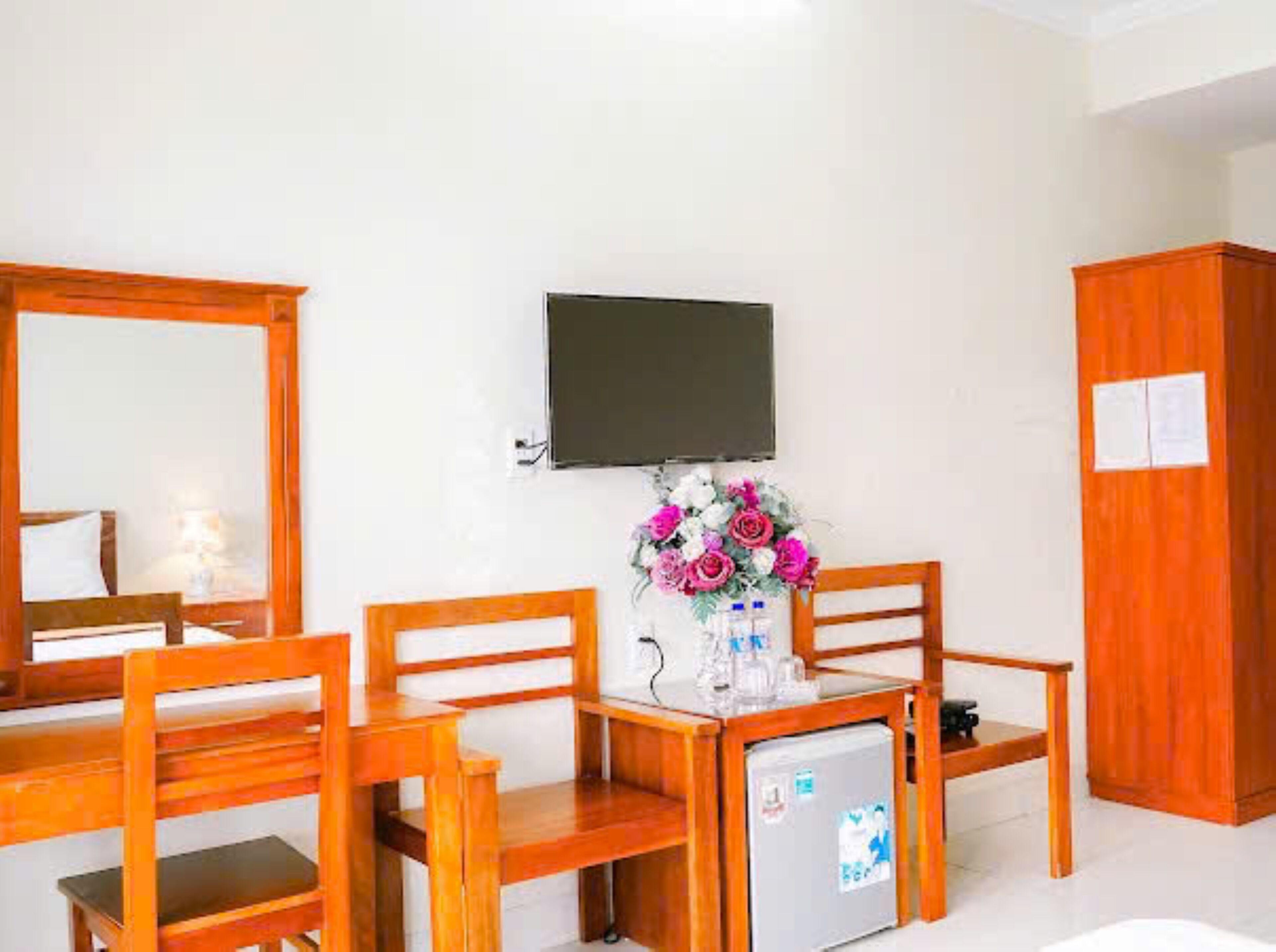 Una stanza con un letto, una scrivania con una sedia, un piccolo frigorifero, una TV a muro e un armadio.