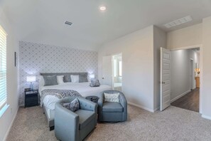 Ein Schlafzimmer mit einem Bett, zwei Sesseln, einem Nachttisch und einer Tür zu einem anderen Raum.