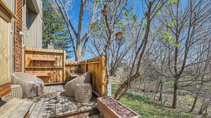 A wooden deck with wicker furniture, a wooden planter, and a view of trees and sky.