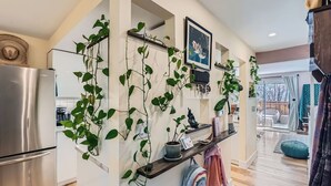 A modern kitchen with a stainless steel refrigerator, wooden shelves with plants, and a view to the dining area.