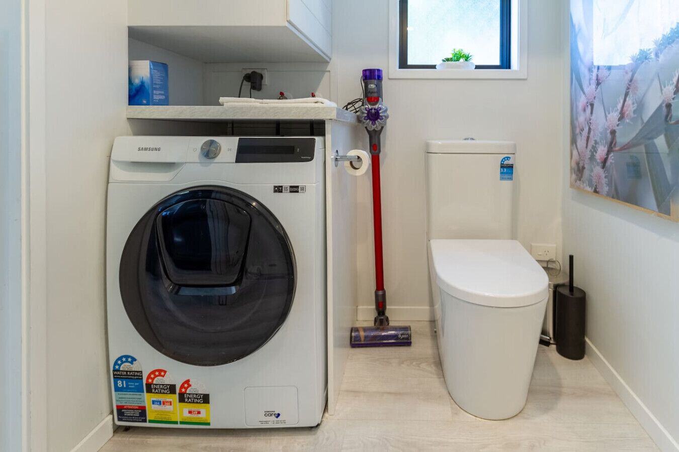Une petite buanderie équipée d’un lave-linge à chargement frontal, de toilettes et d’un balai.