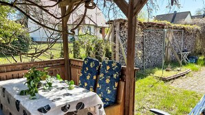 An outdoor patio with a table covered in a white tablecloth with black polka dots, two chairs with blue floral upholstery, and a wooden pergola overhead. - Vacation home Hammel by Interhome (Koserow)