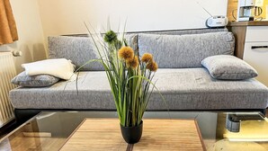 A modern living room with a grey sofa, a glass coffee table, and a potted plant with yellow flowers. - Vacation home Hammel by Interhome (Koserow)