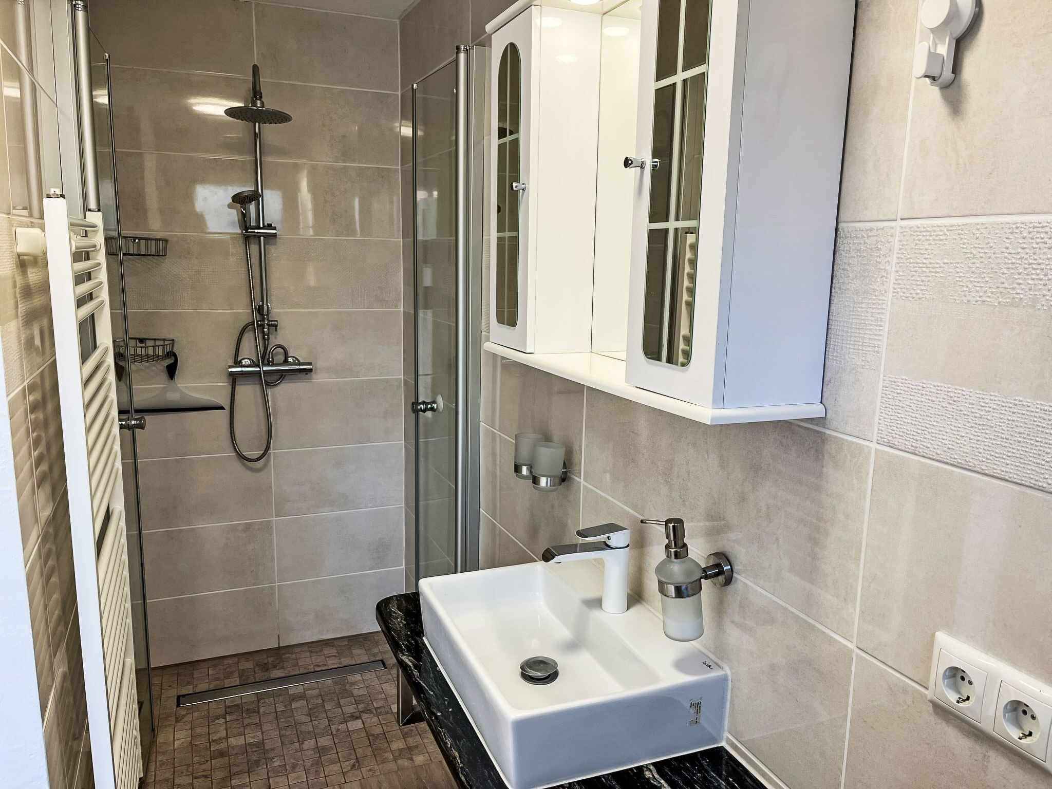 Een moderne badkamer met een douchecabine van glas, een wit wastafelmeubel met een marmeren aanrechtblad, en een wit kastje boven de wastafel.