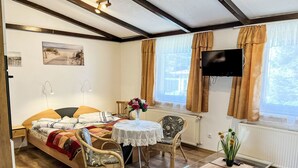 A cozy room with a bed, a small table with a vase, a chair, a TV, and a window with curtains. - Vacation home Hammel by Interhome (Koserow)