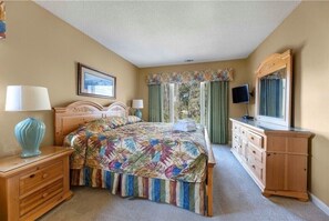 A bedroom with a bed, bedside tables, a dresser, a television, and a window with curtains.