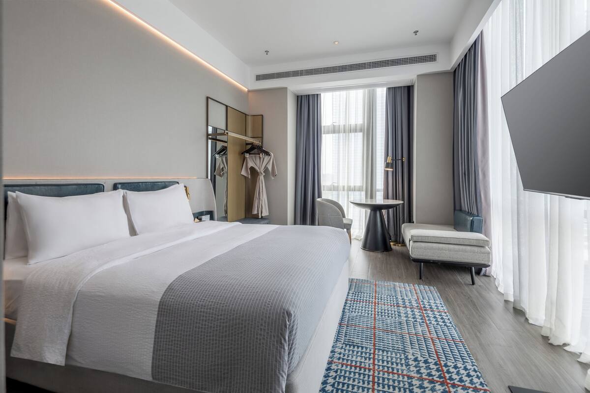 Moderni hotellihuone, jossa on suuri sänky, oleskelualue ja näkymä kaupunkiin.