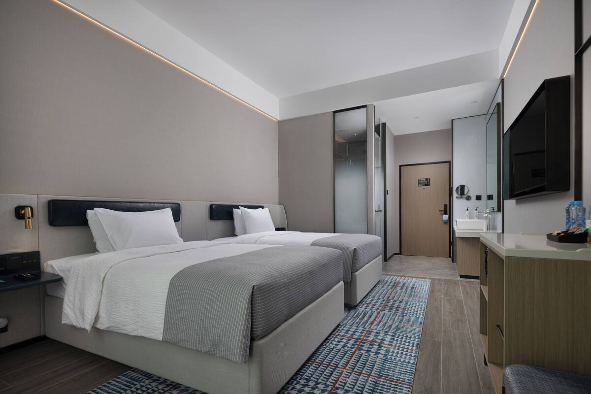 Moderni hotellihuone, jossa on kaksi sänkyä, suuri peili, sisäänrakennettu työpöytä sekä kylpyhuone, jossa on suihku ja wc.