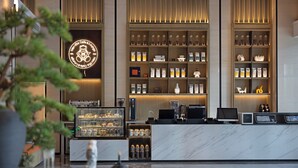 Una cafetería moderna con mostrador de mármol, estantes de granos de café y frascos, y un terminal de pago digital.