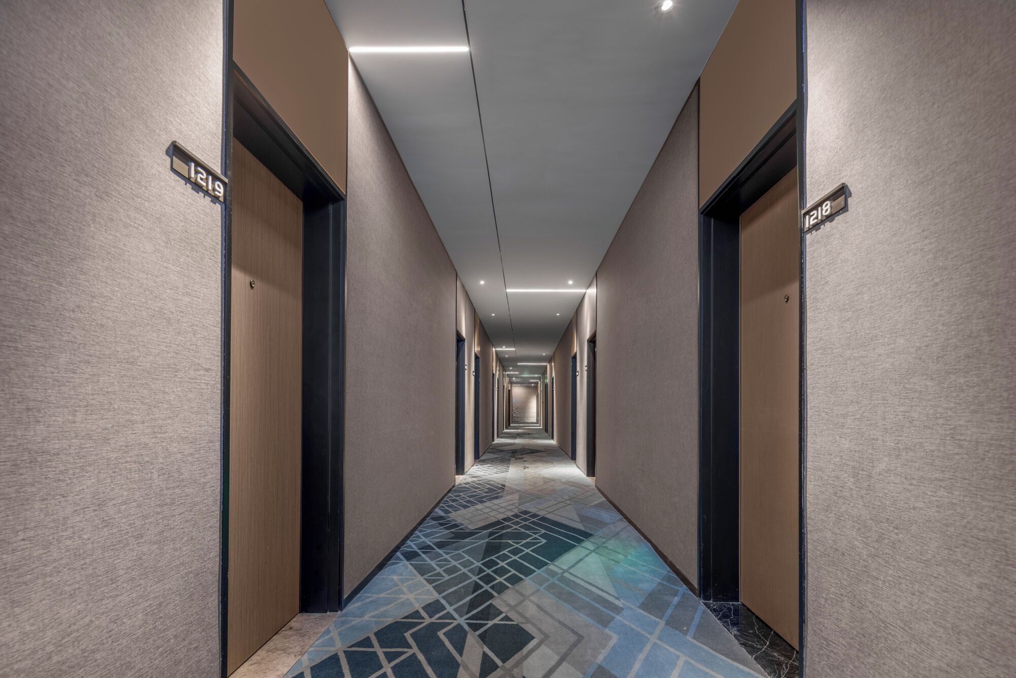 Un largo y estrecho pasillo de hotel con puertas a ambos lados, numeradas 1219 y 1218.