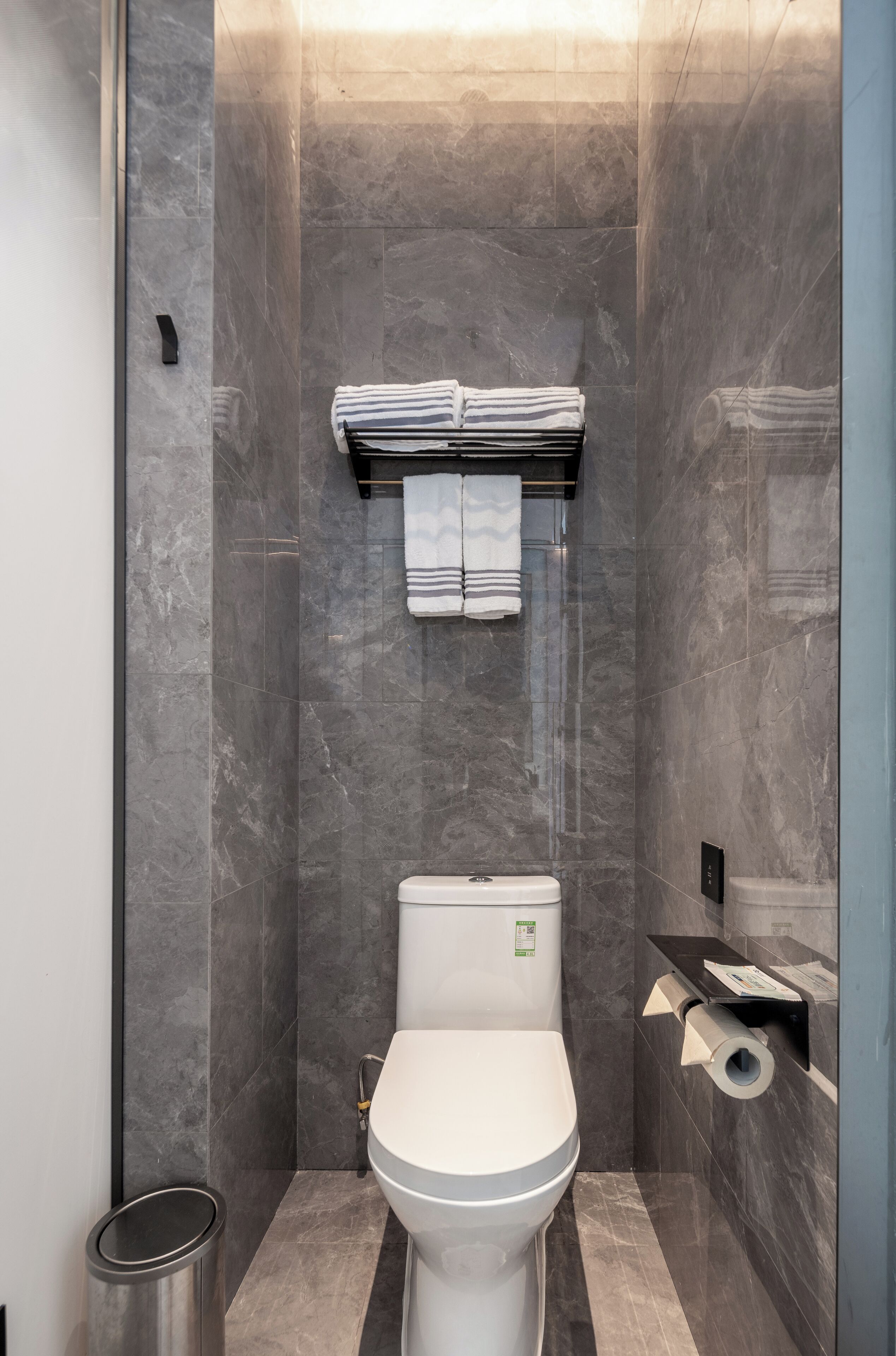 A modern bathroom with a toilet, a trash bin, and a towel rack with towels.