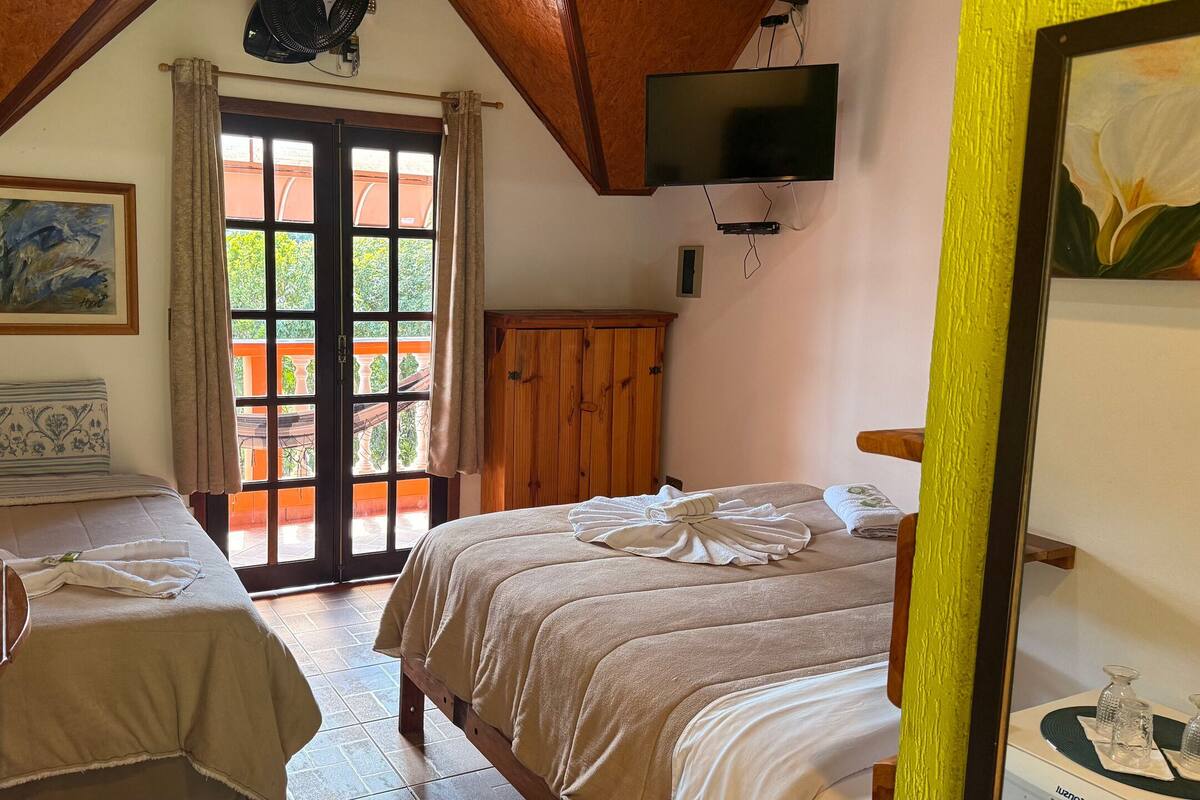 A bedroom with two beds, a TV, a painting, and a window with curtains.