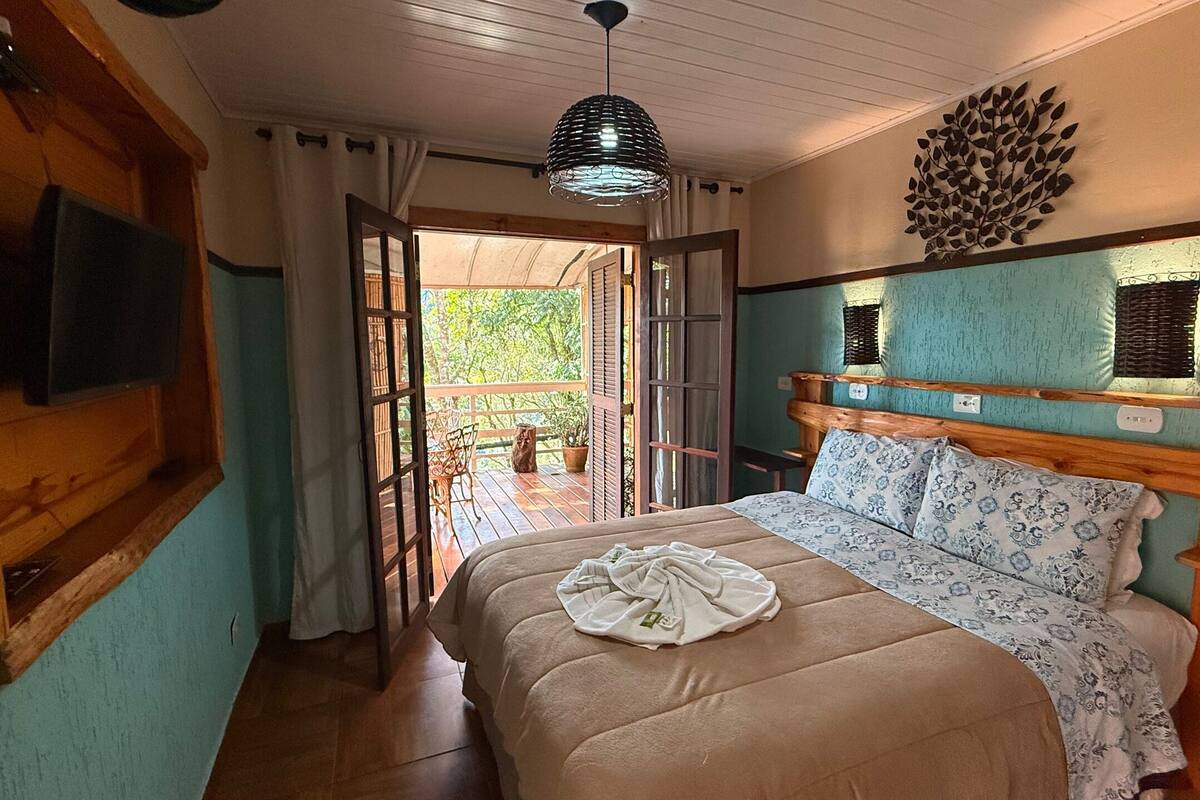 A bedroom with a bed, a TV, a wooden headboard, a ceiling light, and a view of the outdoors.