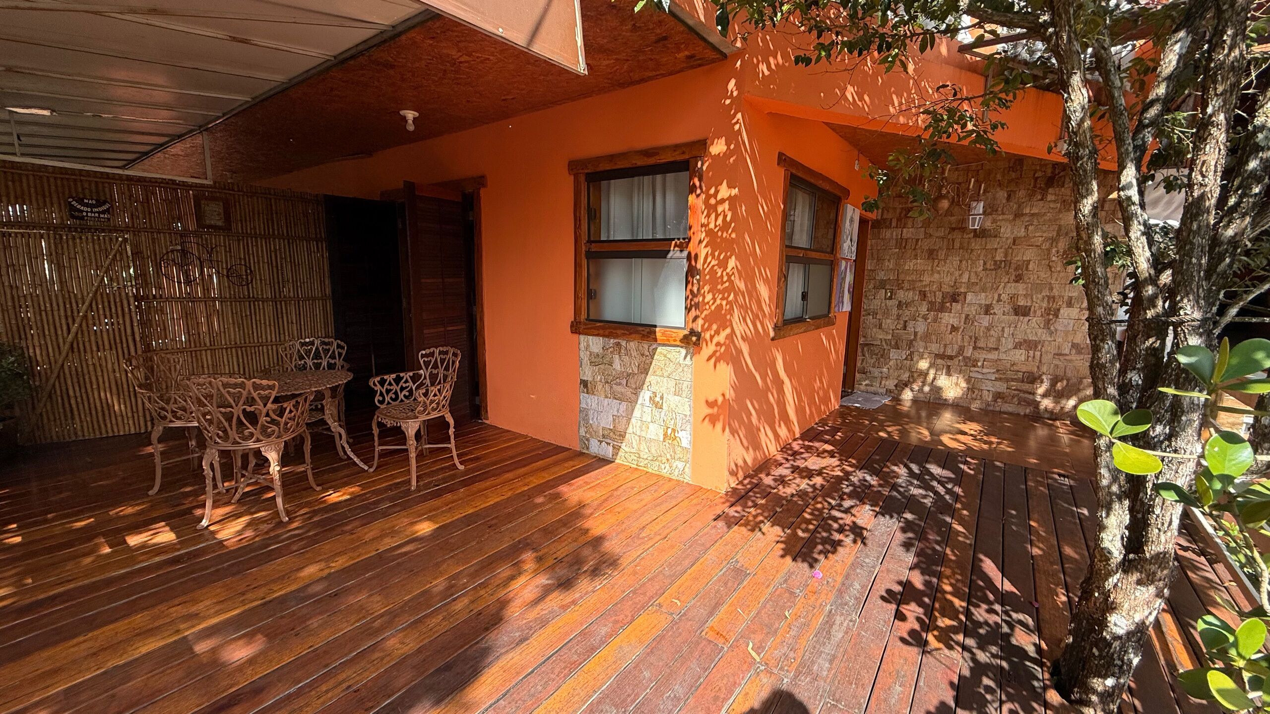 Una terraza de madera con mobiliario exterior, un muro de piedra y un árbol.