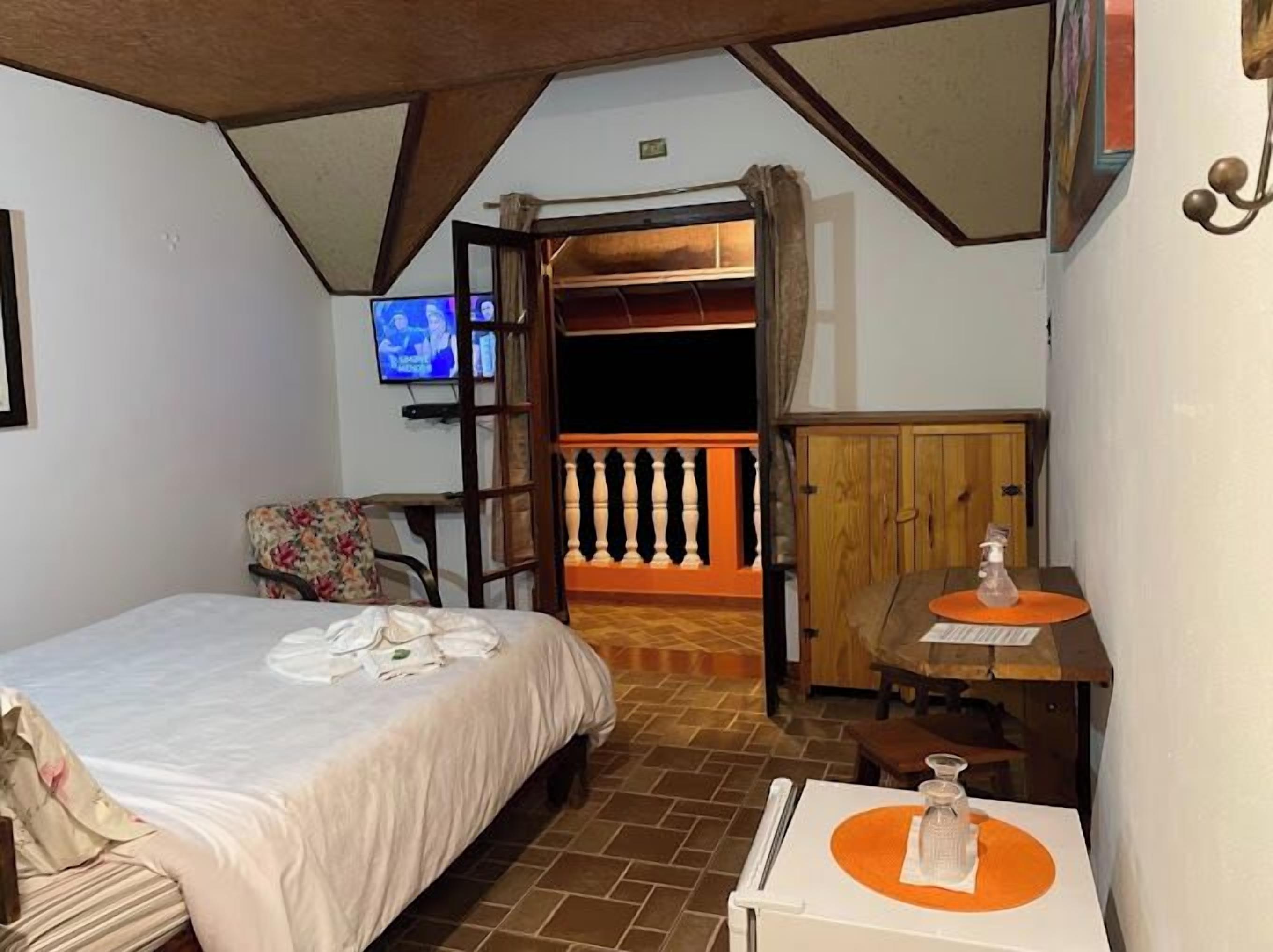 Un dormitorio con cama, televisor, una mesita con una botella y un armario de madera.