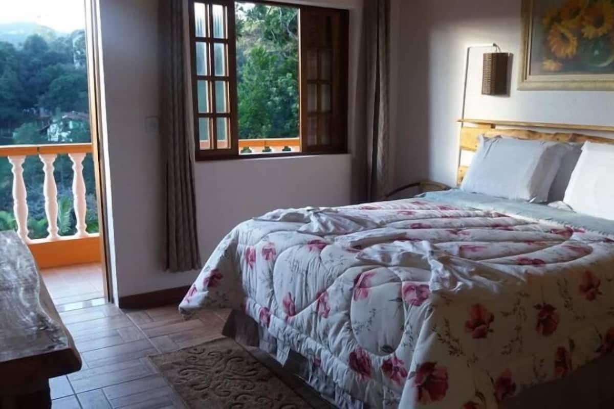 A bedroom with a bed, a window, a balcony, and a painting on the wall.