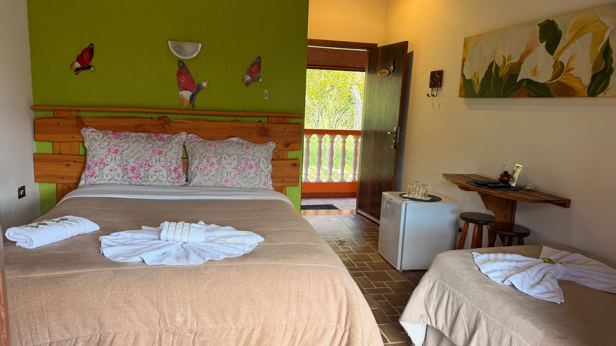 Una habitación de hotel con una cama, dos mesitas de noche, un refrigerador pequeño y un cuadro en la pared.