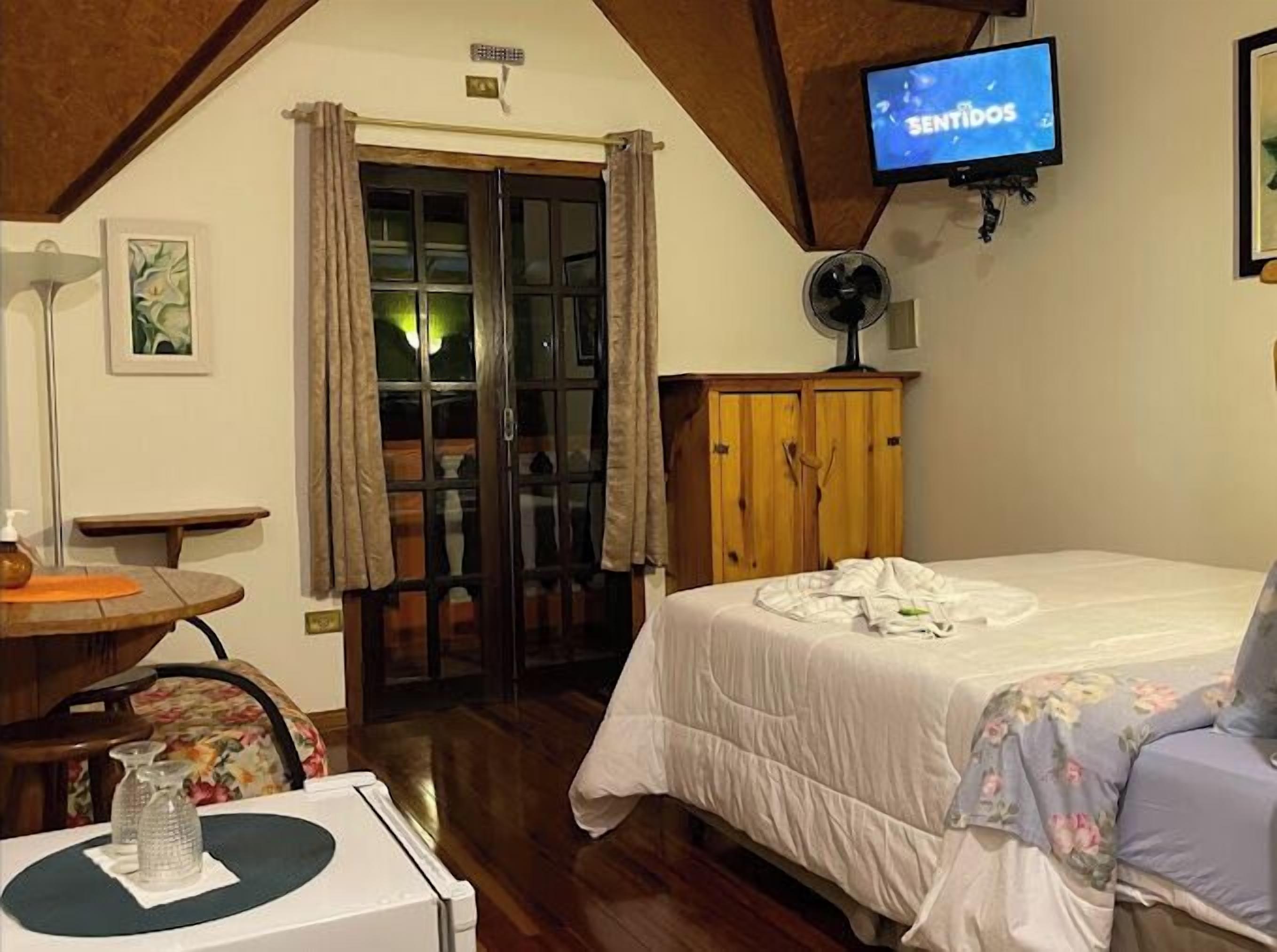A bedroom with a bed, a wooden wardrobe, a television, and a door leading to a balcony.