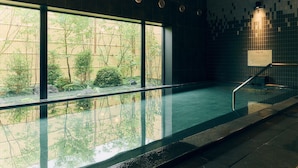 A modern indoor swimming pool with large windows, a tiled wall, and a metal railing.