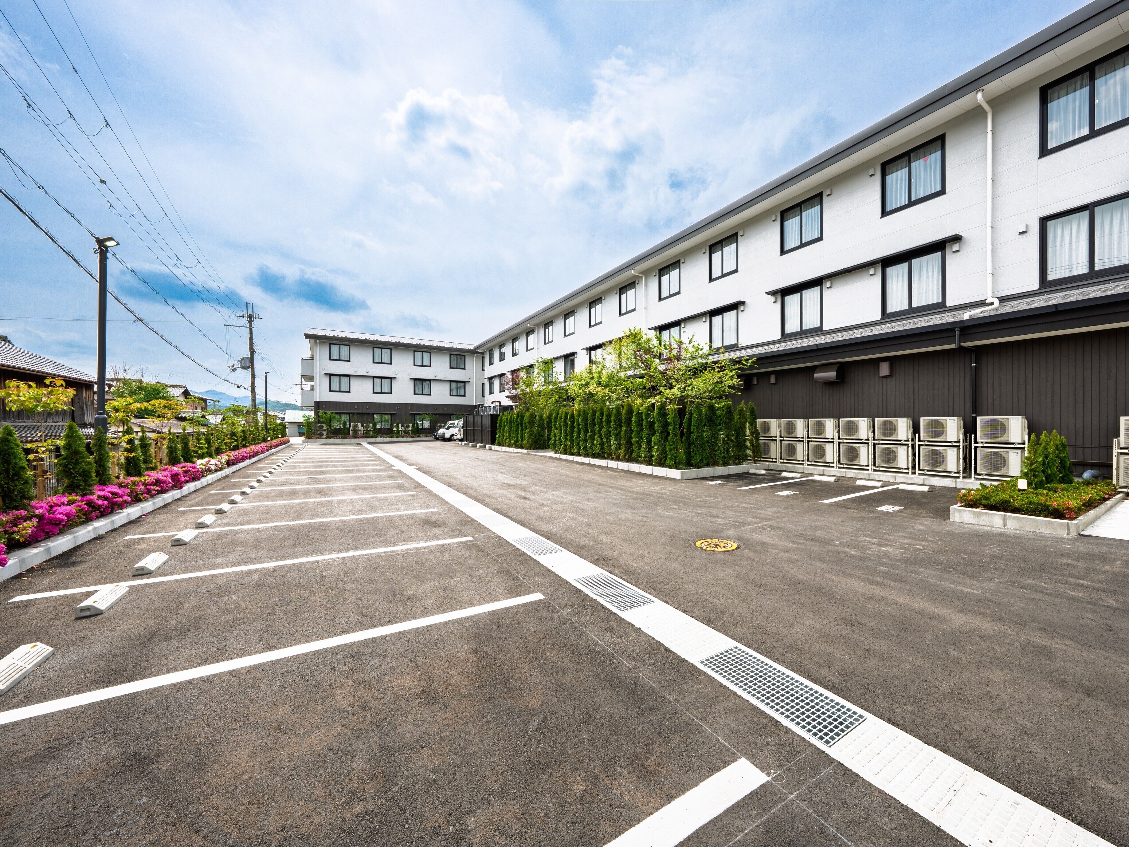A modern hotel with a parking lot, air conditioning units, and a row of trees.