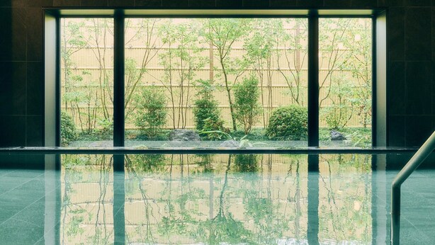 A modern interior with a large window reflecting a garden with trees and a fence.
