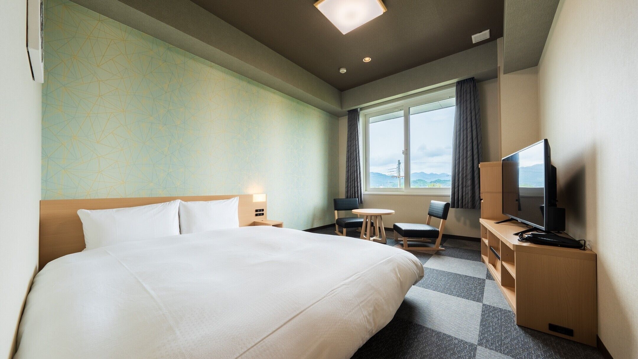 Une chambre d’hôtel avec un grand lit, un bureau avec un ordinateur, une télévision et une fenêtre donnant sur un beau paysage.