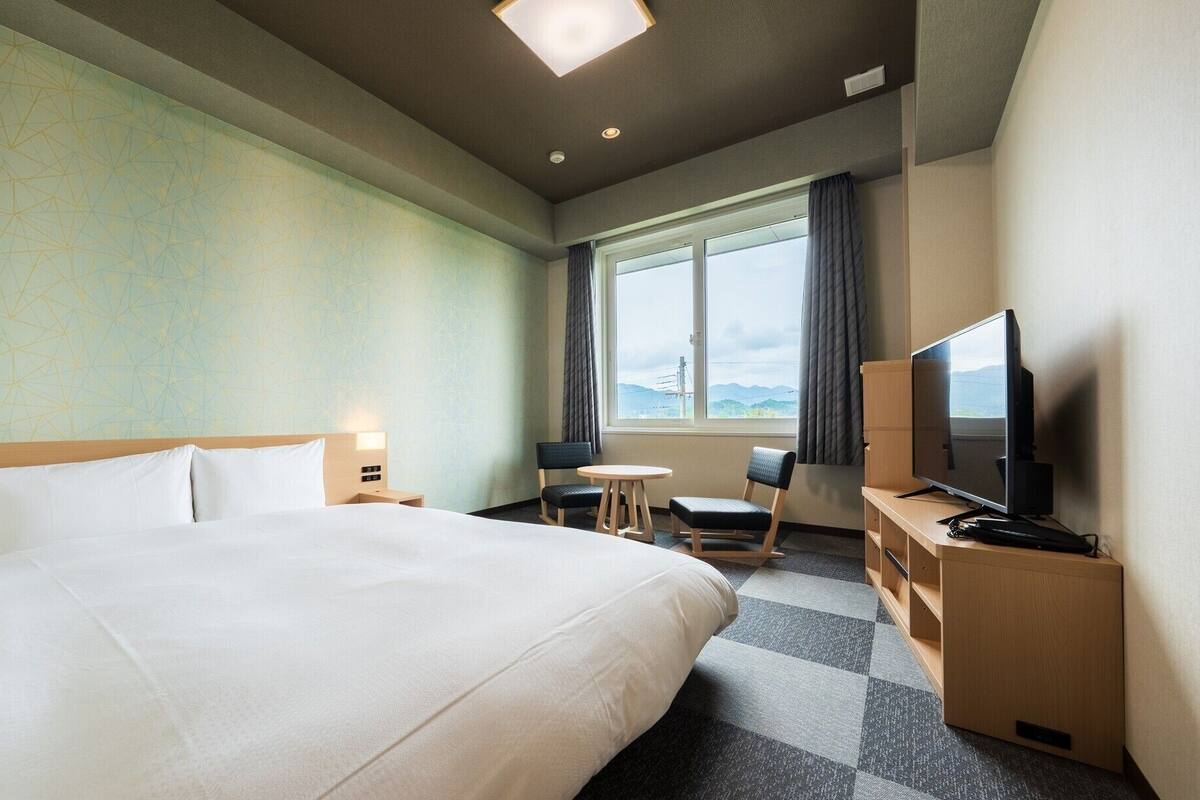 A hotel room with a large bed, a desk with a computer, a TV, and a window with a view.