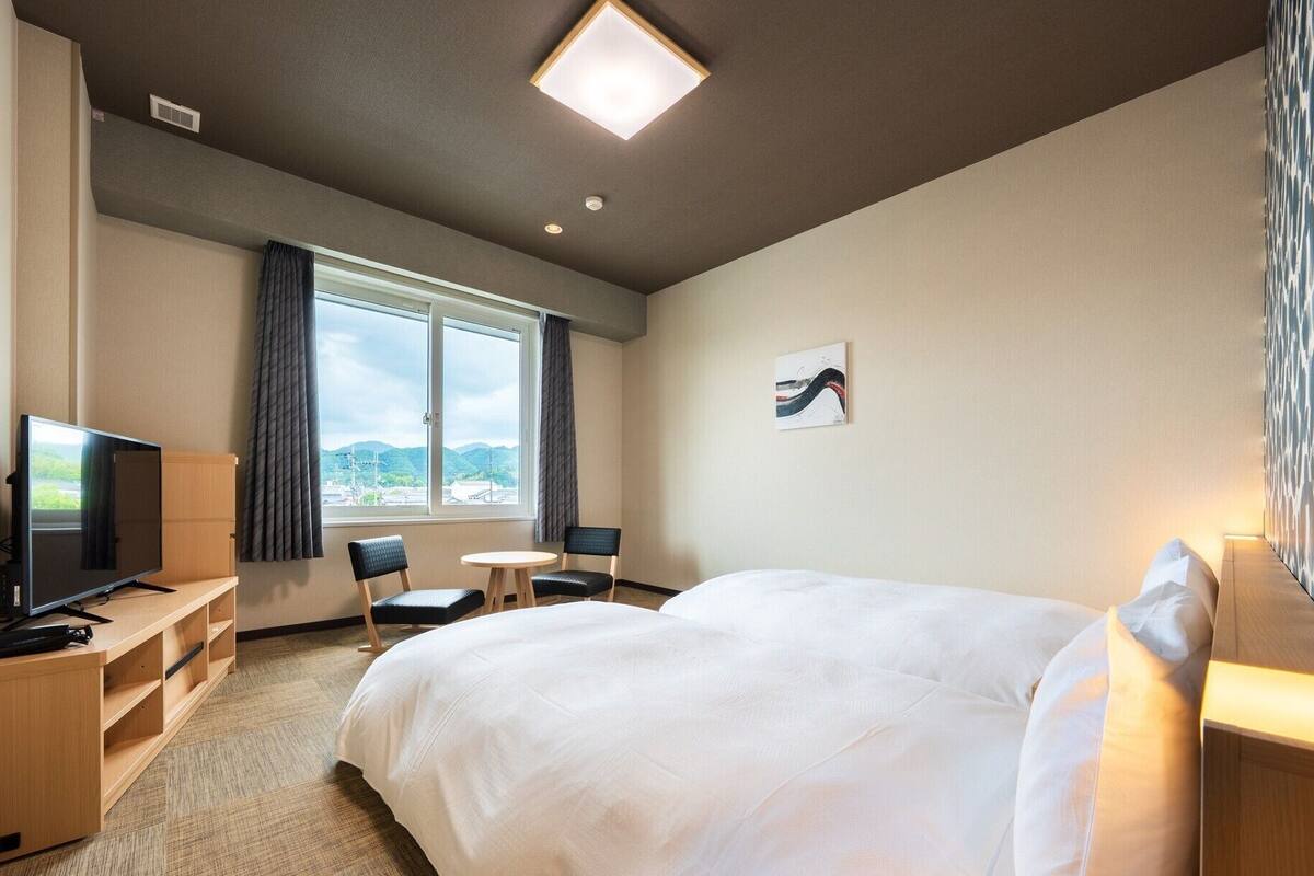 A hotel room with a bed, a TV, a desk, and a chair.