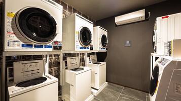 A laundry facility with multiple washing machines and dryers, a tiled floor, and a wall-mounted air conditioning unit.