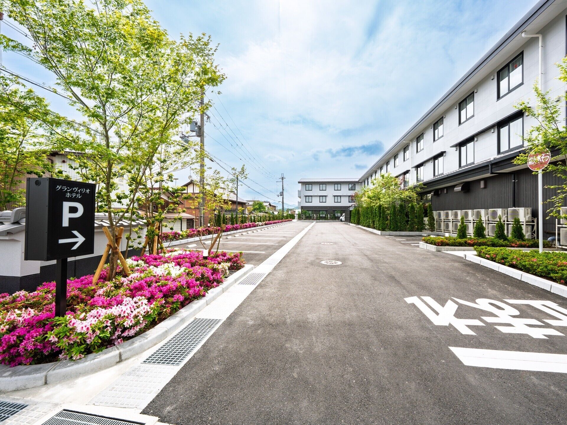 Uma área de estacionamento com placa indicando um hotel, cercada por canteiros de flores e árvores.