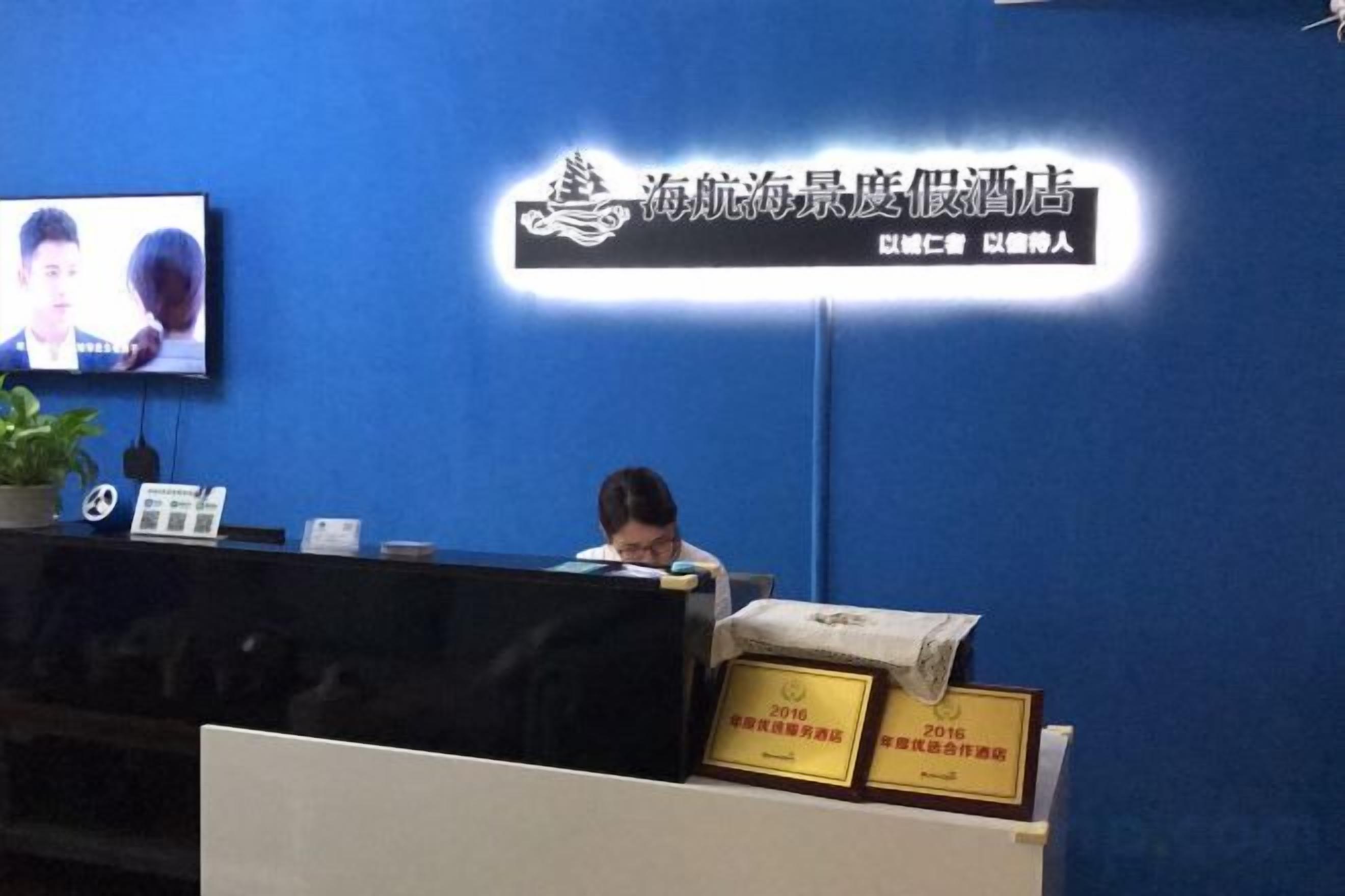 Un mostrador de recepción con una pantalla de televisión, una planta en maceta y certificados enmarcados.
