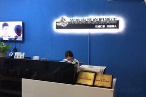A reception desk with a television screen, a potted plant, and framed certificates. - Honghai Bay Haihang Holiday Hotel (Huidong)