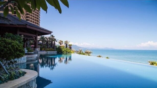 A clear blue infinity pool with a stone border, a wooden gazebo, and palm trees. - Honghai Bay Haihang Holiday Hotel (Huidong)