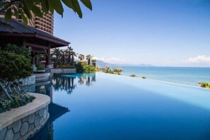 A clear blue infinity pool with a stone border, a wooden gazebo, and palm trees. - Honghai Bay Haihang Holiday Hotel (Huidong)
