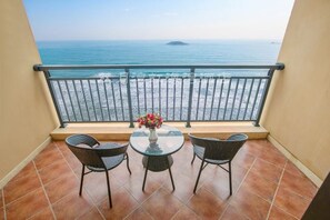 Un balcone con vista sul mare, un tavolo rotondo con sedie e un vaso di fiori.