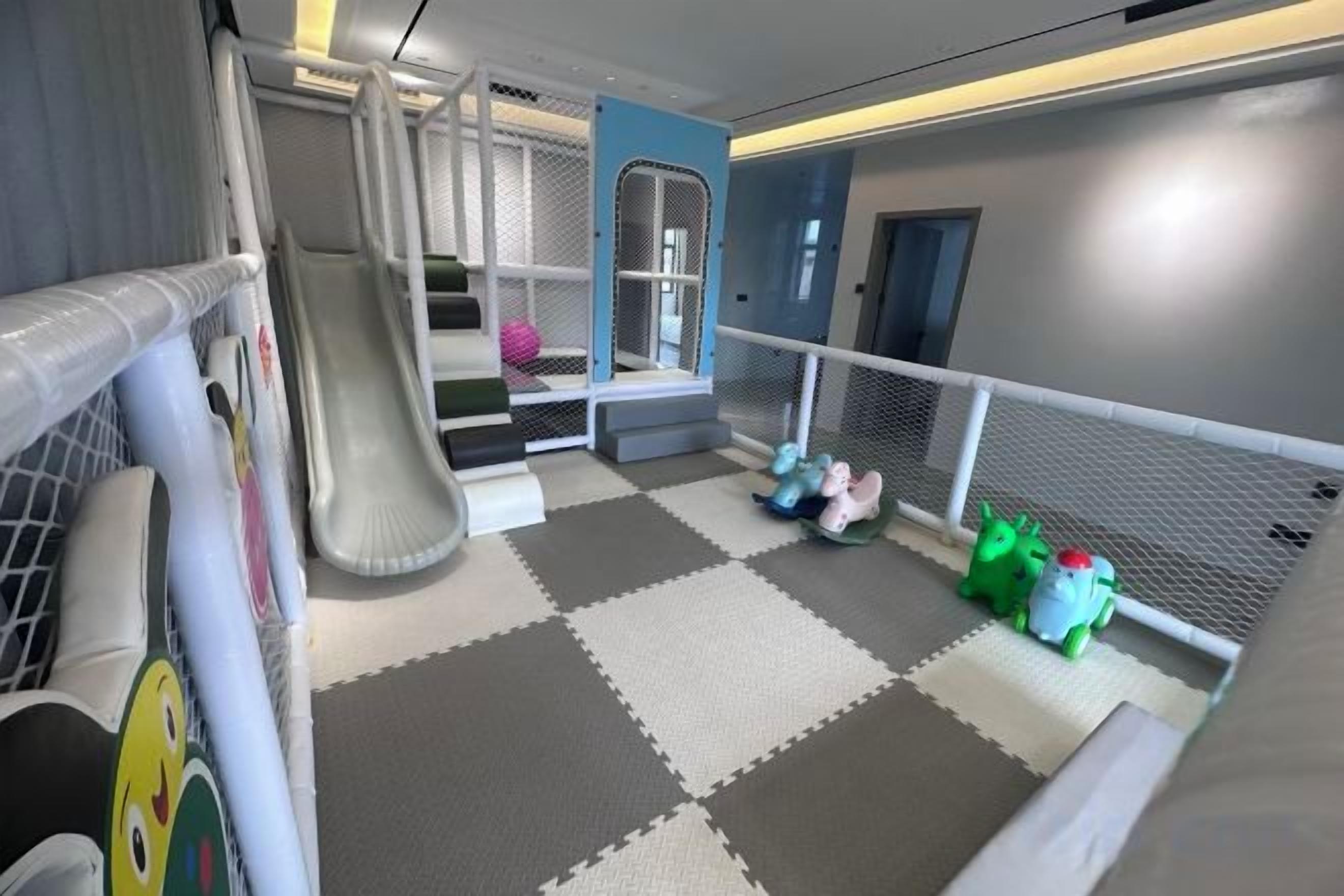 A children's play area with a slide, soft play mats, and a netted play zone.