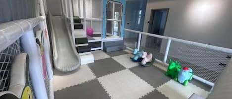 A children's play area with a slide, soft play mats, and a netted play zone.