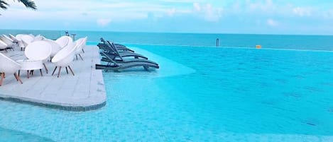 A poolside area with lounge chairs and a clear view of the ocean.