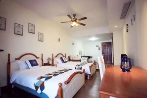 Habitación de hotel con dos camas, cabecera de madera, ventilador de techo y una mesa de madera con una linterna.