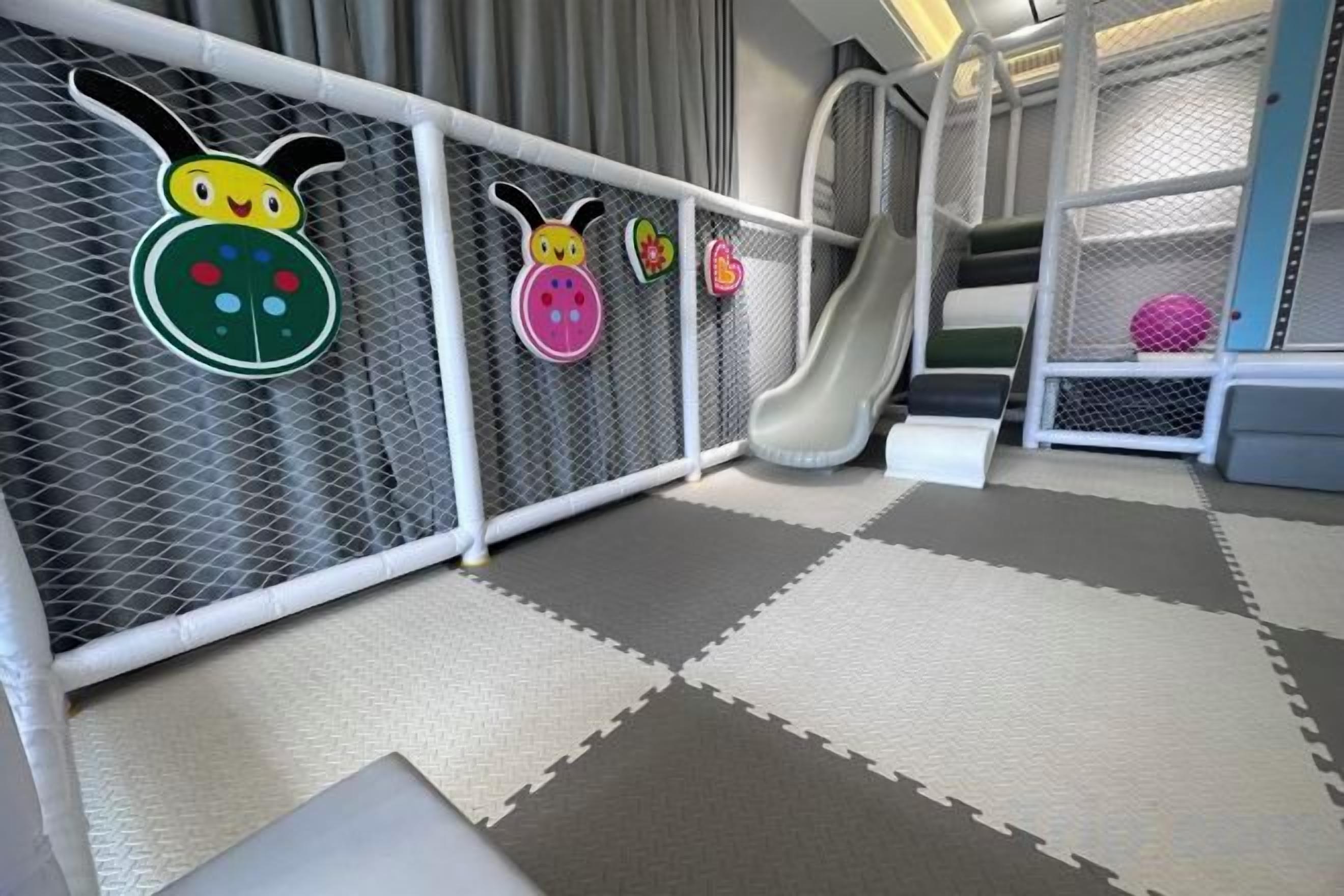 A play area with a slide, padded flooring, and safety netting.