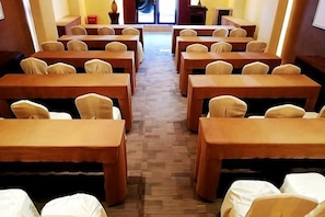 A conference room with rows of tables and chairs, a carpeted floor, and a view of the outdoors through a door.