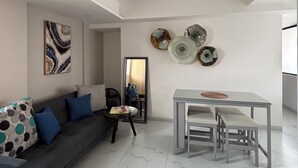 A modern living room with a grey sofa, a glass dining table with chairs, and a large mirror. - Departamento de una habitación en Roma Sur CDMX (Ciudad de México)