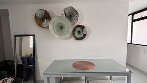 A modern dining area with a glass table and two chairs, a large mirror, and decorative wall art. - Departamento de una habitación en Roma Sur CDMX (Ciudad de México)