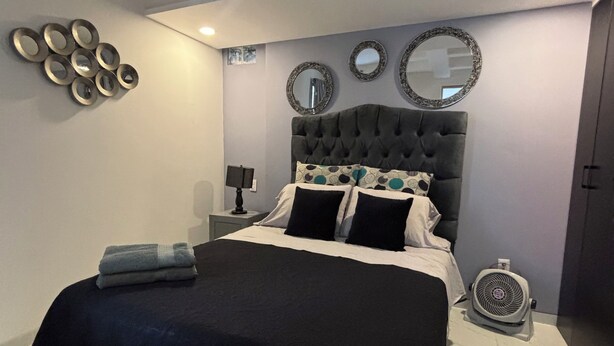 A modern bedroom with a tufted headboard, a bed with black and white bedding, a bedside table with a lamp, and a wall-mounted fan. - Departamento de una habitación en Roma Sur CDMX (Ciudad de México)