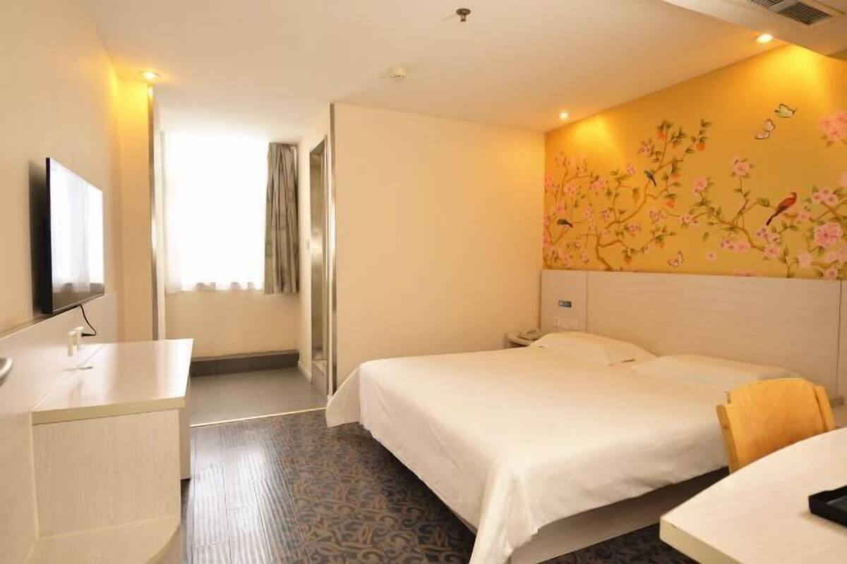 Ein Hotelzimmer mit zwei Betten, einem Schreibtisch, einem Fernseher und einer Wand mit floralen Bildern.