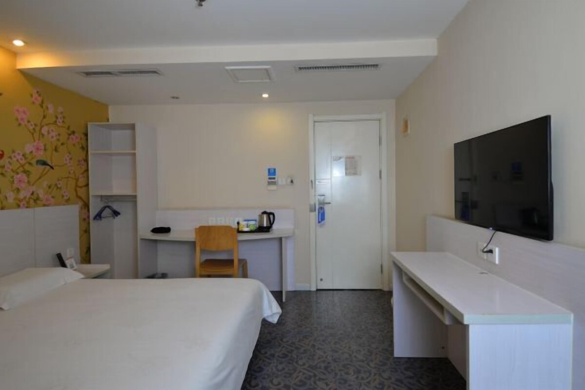 A hotel room with a bed, a desk, a chair, a television, and a wardrobe.