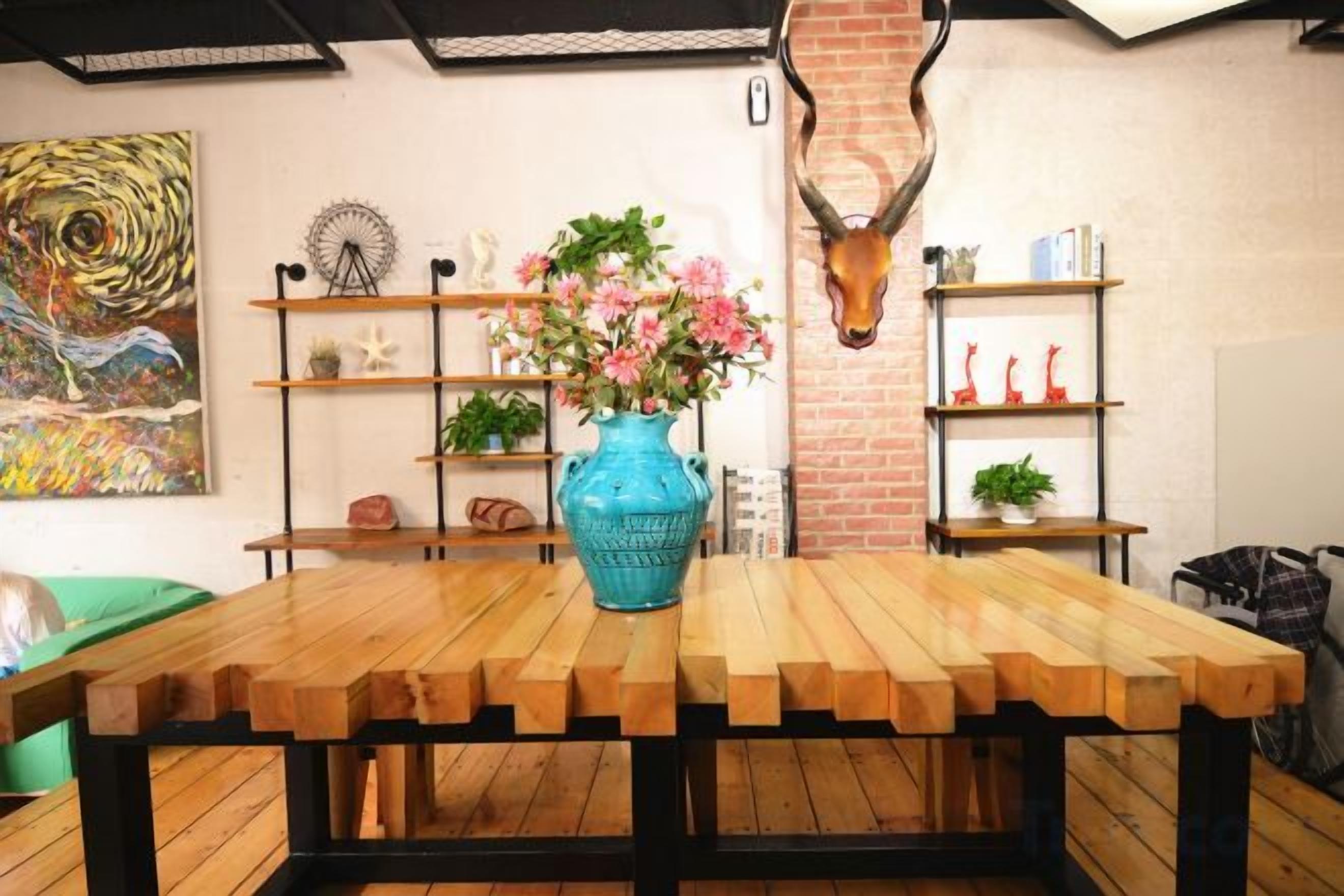 A wooden dining table with a blue vase of flowers, surrounded by shelves with decorative items and a wall-mounted animal head.