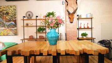A wooden dining table with a blue vase of flowers, surrounded by shelves with decorative items and a wall-mounted animal head.