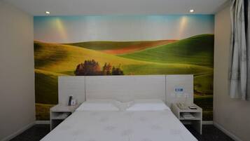 A bedroom with a large mural of rolling hills, a bed with a white headboard, two bedside tables, and a nightstand with a phone.