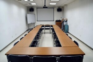 Una sala de conferencias con una mesa larga, sillas, una pizarra, una pantalla de proyector y un atril.